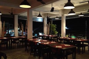 An indoor dining area with tables and chairs, ceiling fans, and pendant lighting.