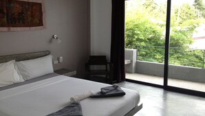 Habitación de hotel con cama, una silla, ventana con vistas a follaje y un cuadro en la pared.