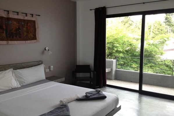 Habitación de hotel con cama, una silla, ventana con vistas a follaje y un cuadro en la pared.