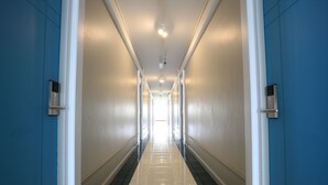 Um corredor comprido e estreito com paredes azuis e detalhes brancos, que leva a uma saída iluminada.
