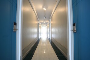 A long, narrow hallway with blue walls and white trim, leading to a bright exit.