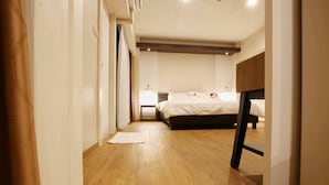 Quarto com piso de madeira, cama com roupa de cama branca, mesa de cabeceira e luminária pendente.
