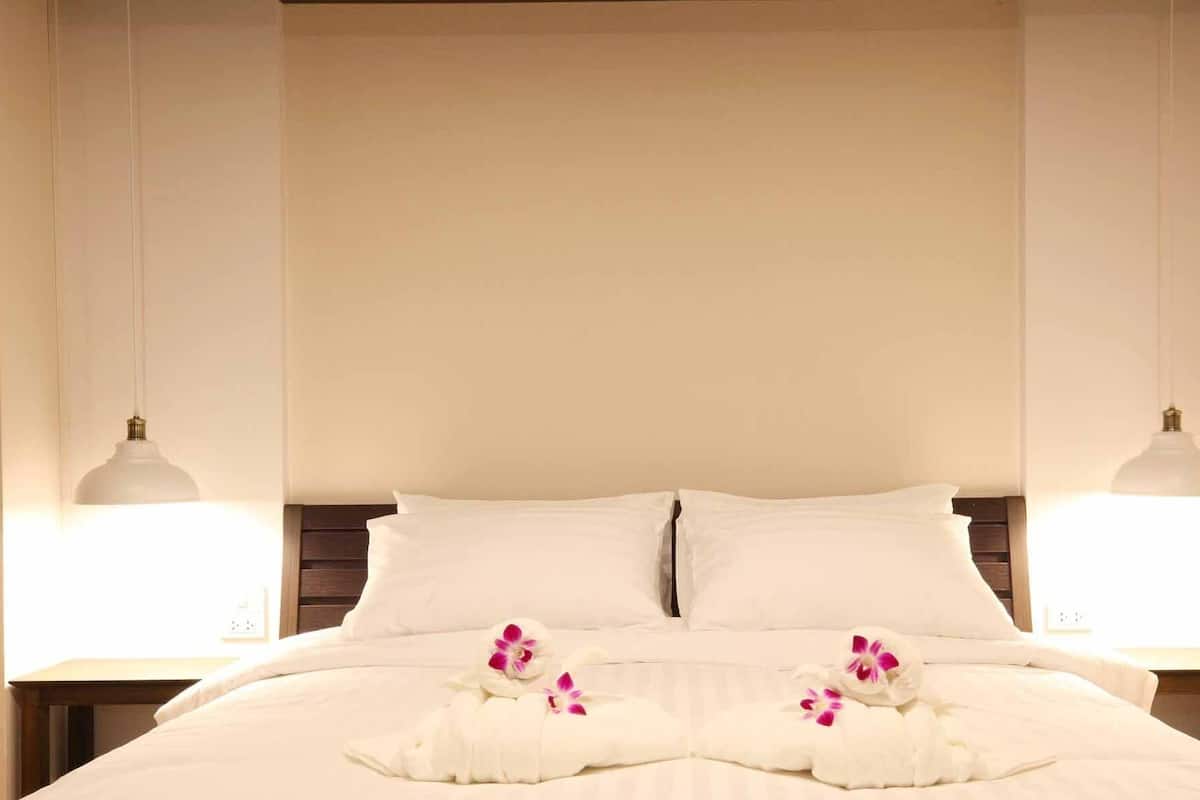 A neatly made bed with white linens and pink orchid flowers, two bedside lamps, and a wooden headboard.