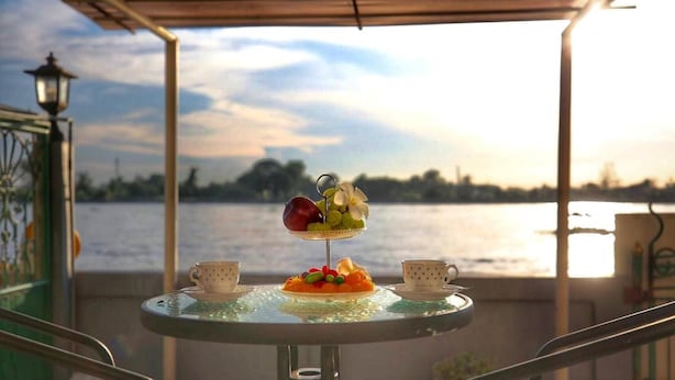 Uma mesa com uma cesta de frutas e duas xícaras, com vista para a paisagem costeira.