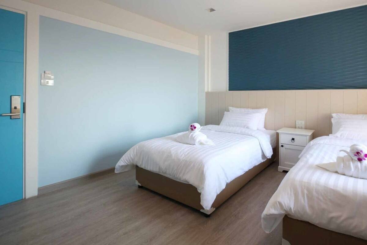 A hotel room with two beds, a blue door, and a large blue wall.