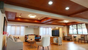 Uma sala de estar espaçosa com teto de madeira, televisão e área de estar com sofás e poltronas.