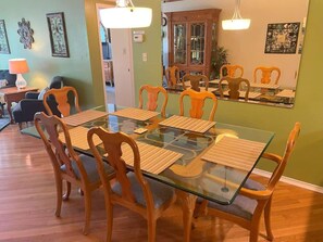 Uma sala de jantar com mesa de vidro, cadeiras de madeira e um armário ao fundo.