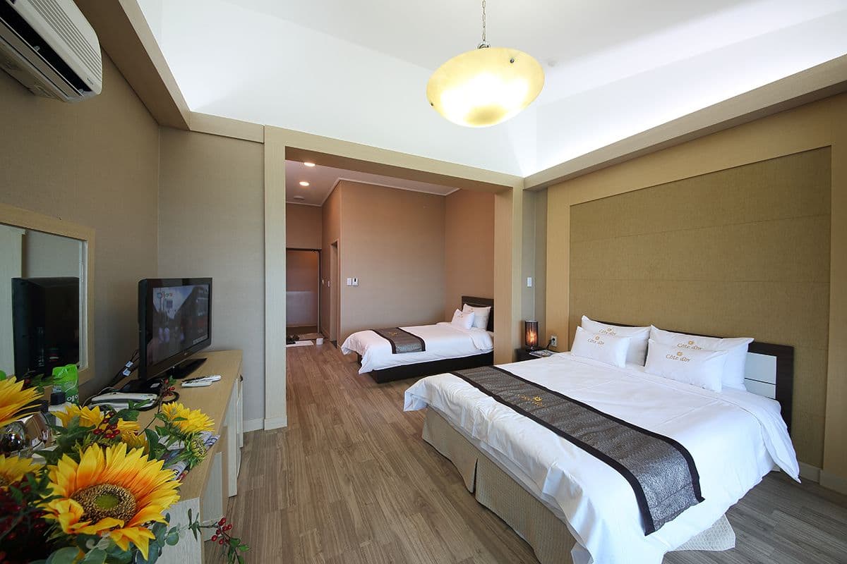 Une chambre d’hôtel avec un grand lit, une télévision, un bureau avec un ordinateur et un vase rempli de tournesols.