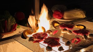 Een barbecue met verschillende vleessoorten en groenten die boven een open vuur garen.