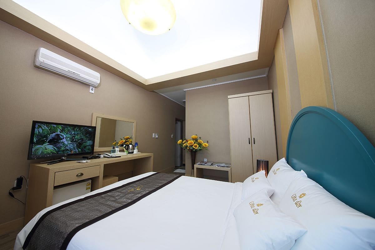 Une chambre d’hôtel comprenant un lit, un bureau avec une télévision, une armoire et une lucarne.