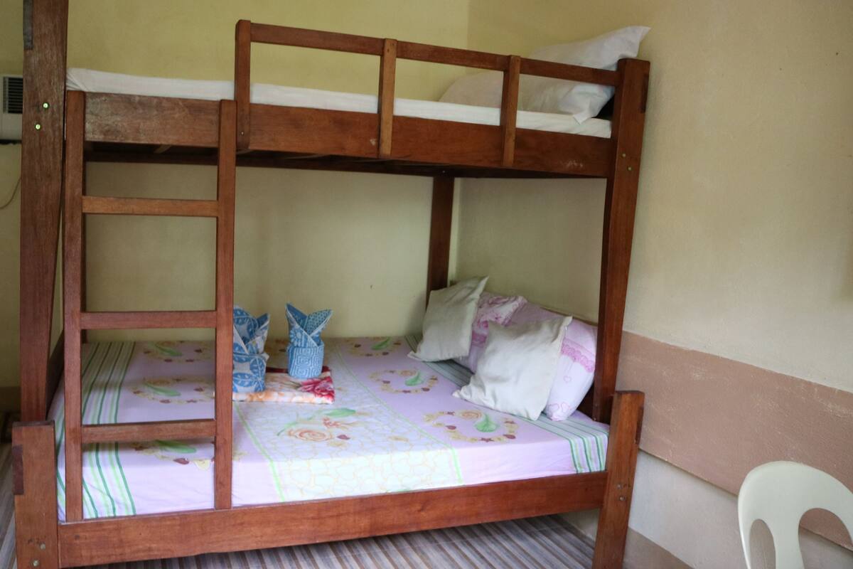Una cama litera con estructura de madera, almohada blanca y colcha estampada con motivos florales.