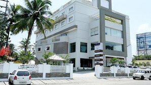 Un edificio moderno de varios pisos con fachada blanca, múltiples balcones y un letrero que indica un restaurante y una tienda.