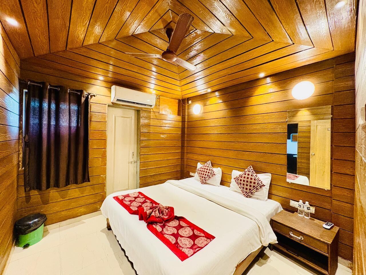 A wooden-paneled room with a bed, a nightstand, a mirror, and a ceiling fan.