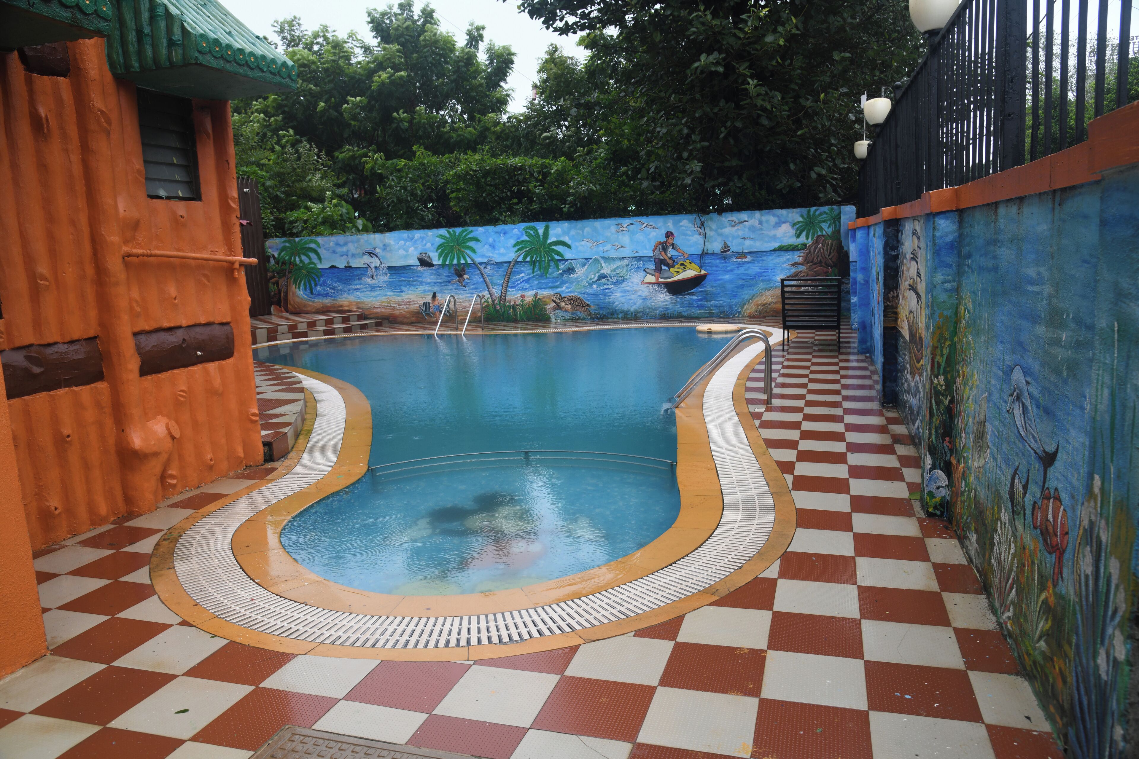 Una piscina con suelo a cuadros, rodeada de murales y una estructura de madera.