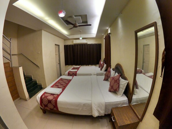 A hotel room with a large bed, a wooden nightstand, a mirror, a ceiling fan, and a staircase. - Hill Forest Resort Lonavala (Mawal)