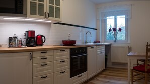 Una cucina compatta con mobili bianchi, una moka rossa, un lavello e una finestra con fiori.