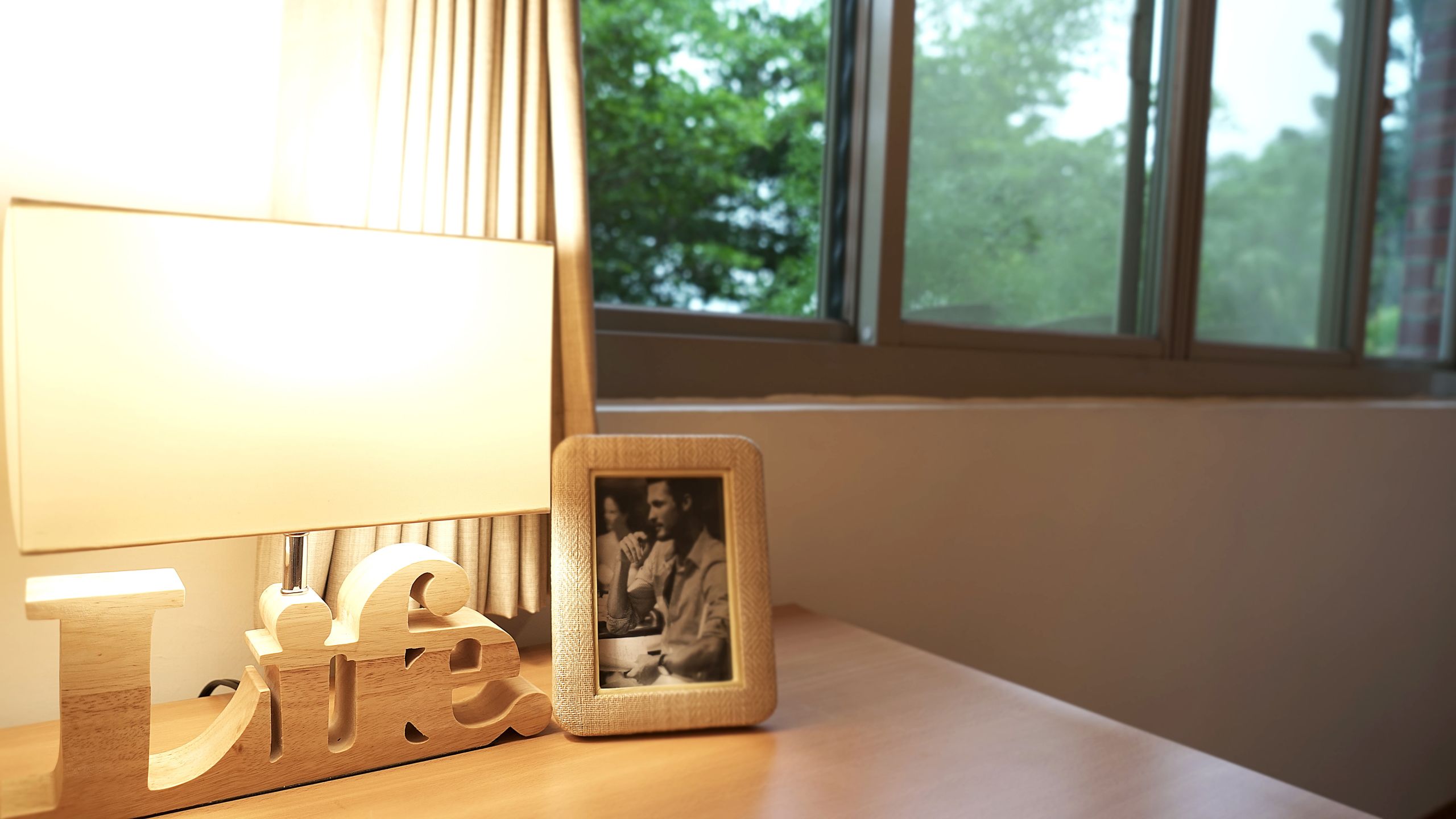 A bedside table with a lamp, a wooden letter 'L' and 'E' block, and a framed photo.