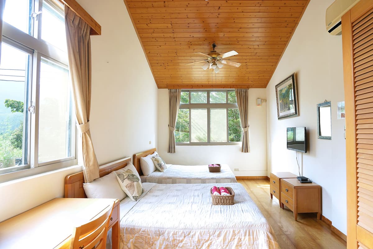Quarto com duas camas, ventoinha no teto, televisão e janela com cortinas.