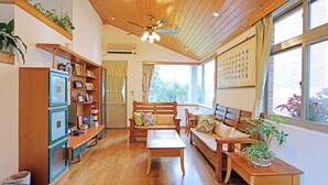 Un salón acogedor con muebles de madera, un ventilador de techo y un amplio ventanal con cortinas.