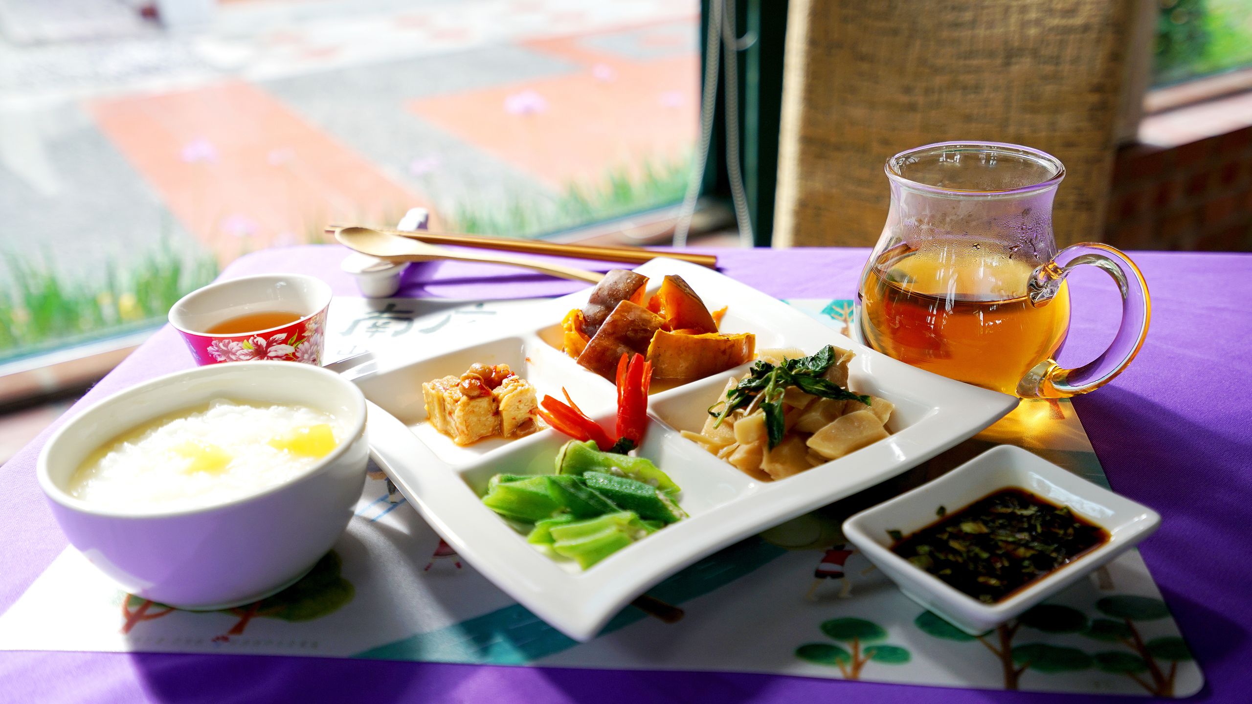 Une table dressée avec un repas composé de différents plats, une tasse de thé et un petit bol de sauce.