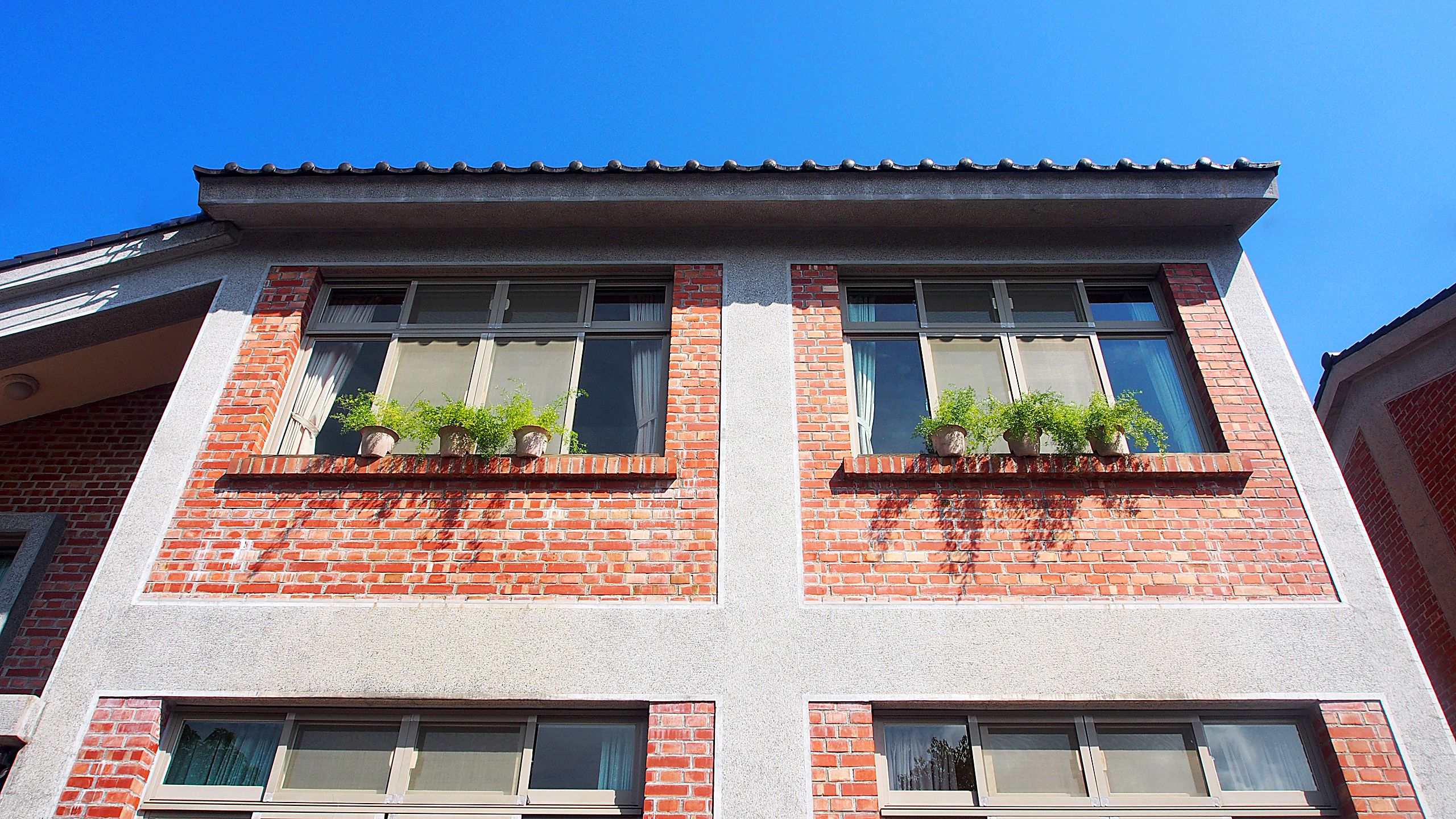 A two-story building with red brick facade, multiple windows with shutters, and potted plants on the windowsills.