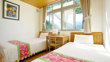 A room with two beds, a desk, and a chair. There is a window with curtains, and a painting on the wall.
