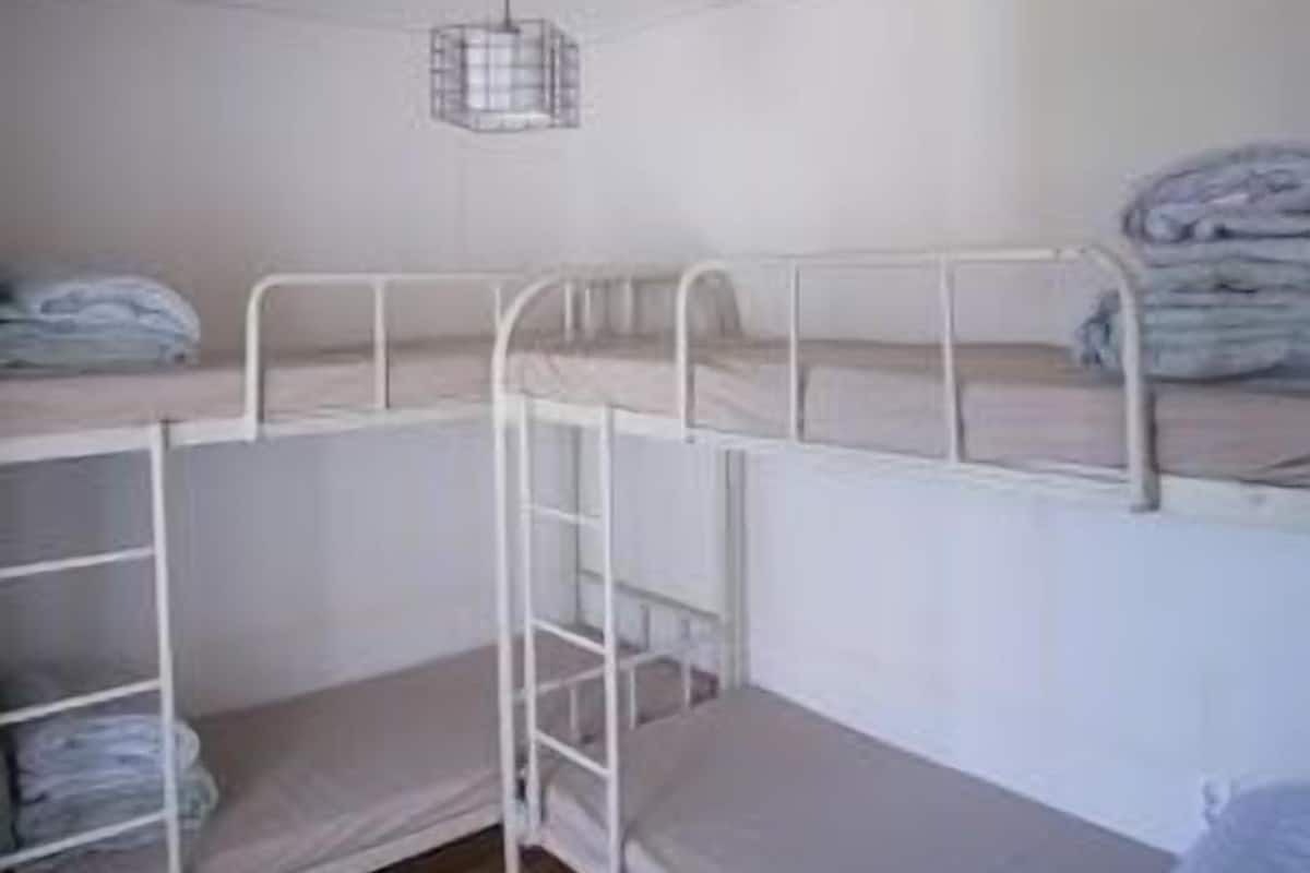 A bunk bed room with a metal ladder, a hanging light fixture, and a wooden floor.