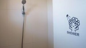 A shower area with a wall-mounted showerhead and a hand shower. - Lucidbonbon - Hostel (Seogwipo)
