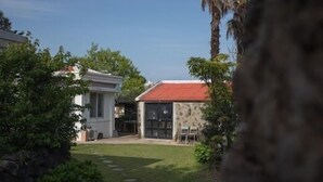 A residential property with a red-roofed building, a white building with large windows, and a well-maintained lawn with stepping stones. - Lucidbonbon - Hostel (Seogwipo)