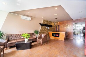 A hotel reception area with a reception desk, a sofa, chairs, and a potted plant.