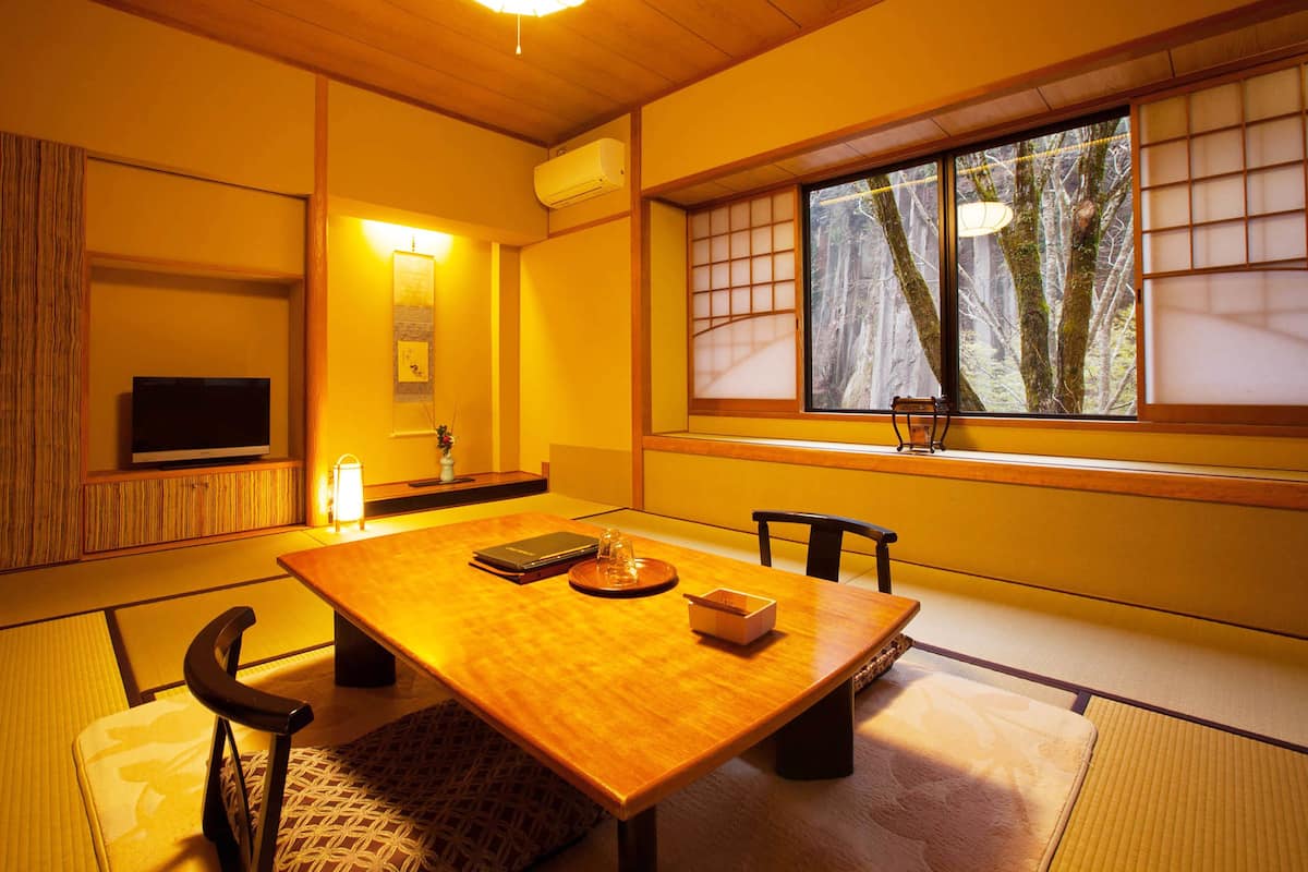 A traditional Japanese room with tatami flooring, a low table, and a television on a shelf.