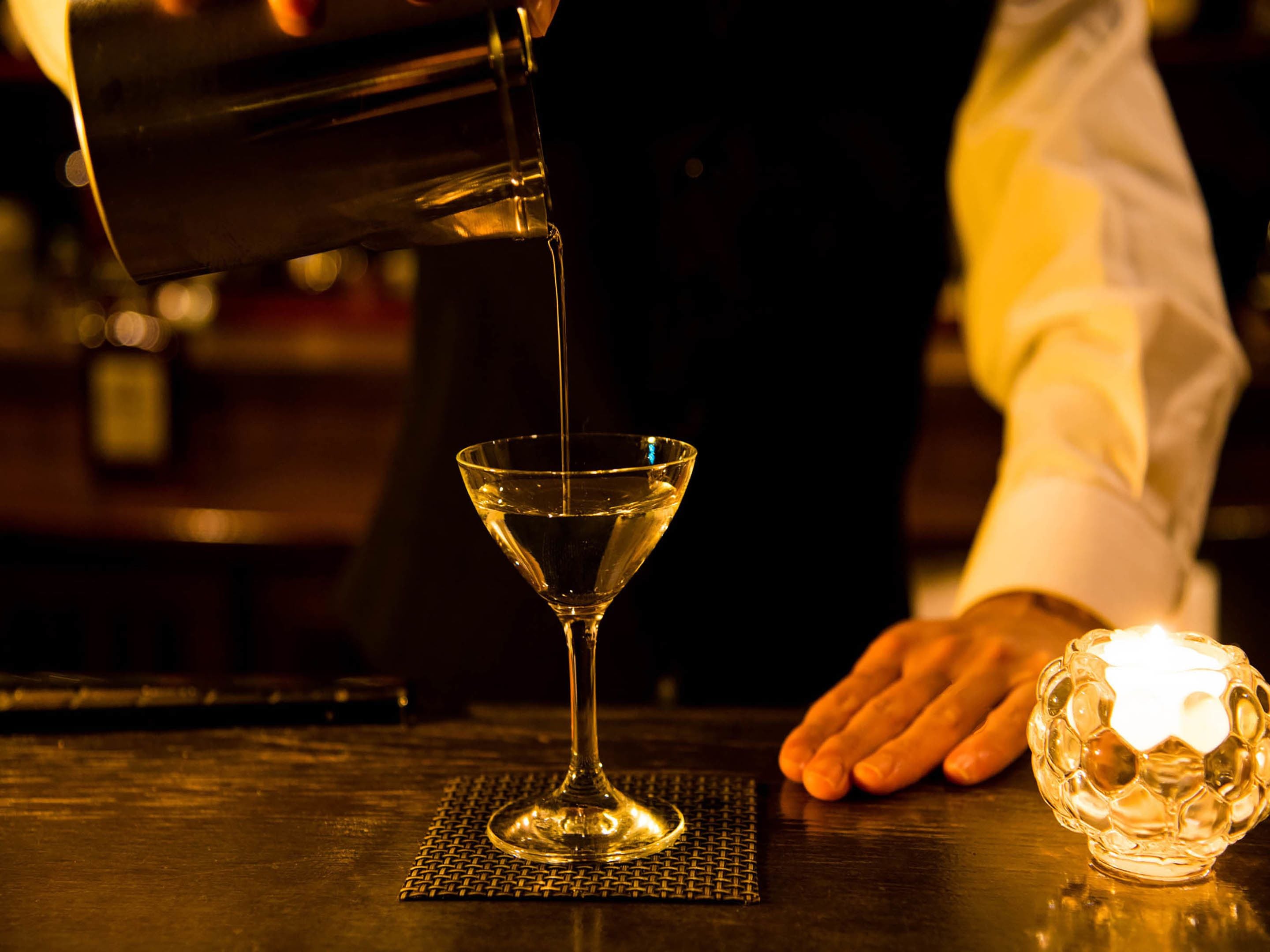 A bartender pouring a clear liquid into a martini glass on a bar counter.