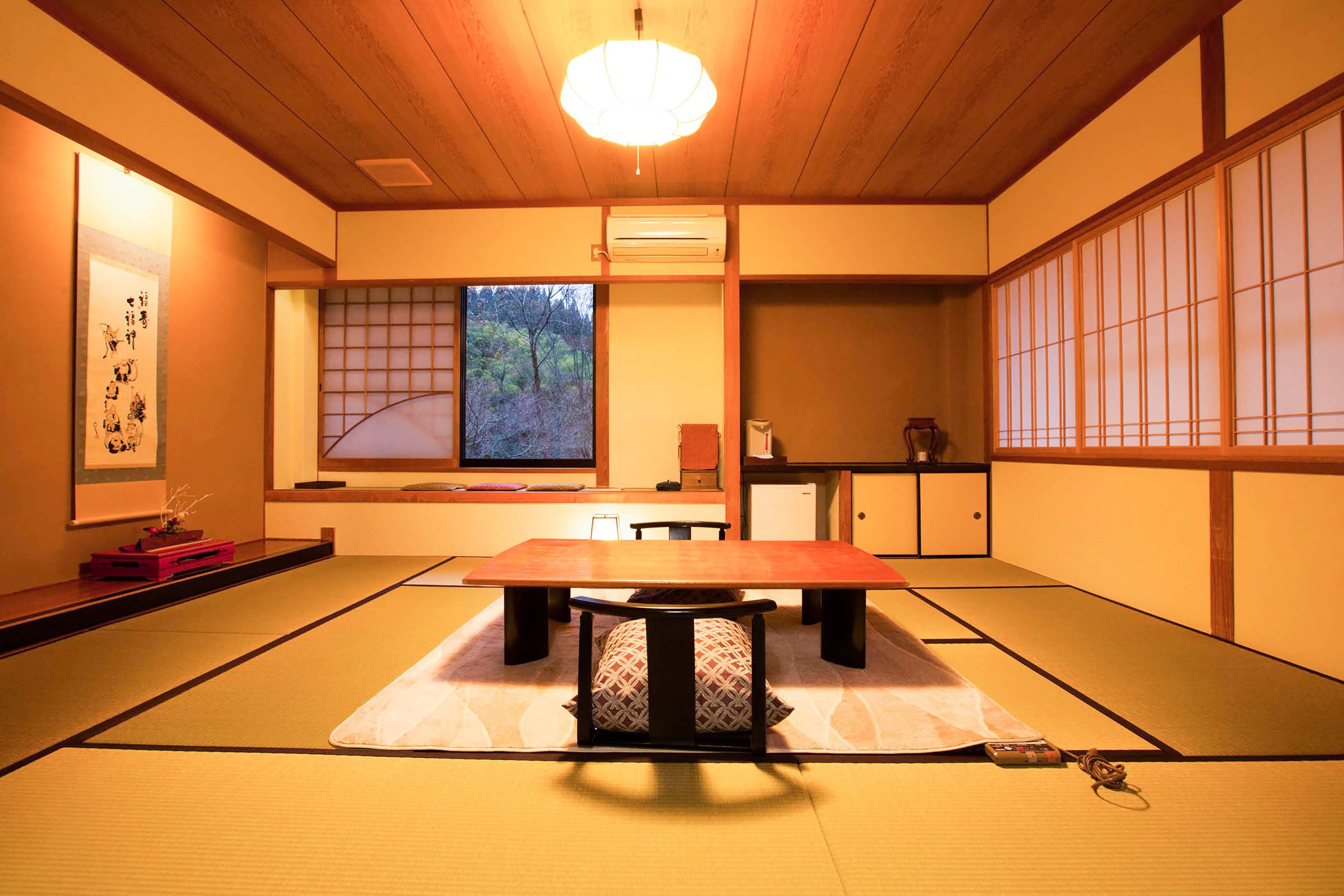 A traditional Japanese room with tatami flooring, a low table with cushions, a sliding door with a view of trees, and a ceiling fan.