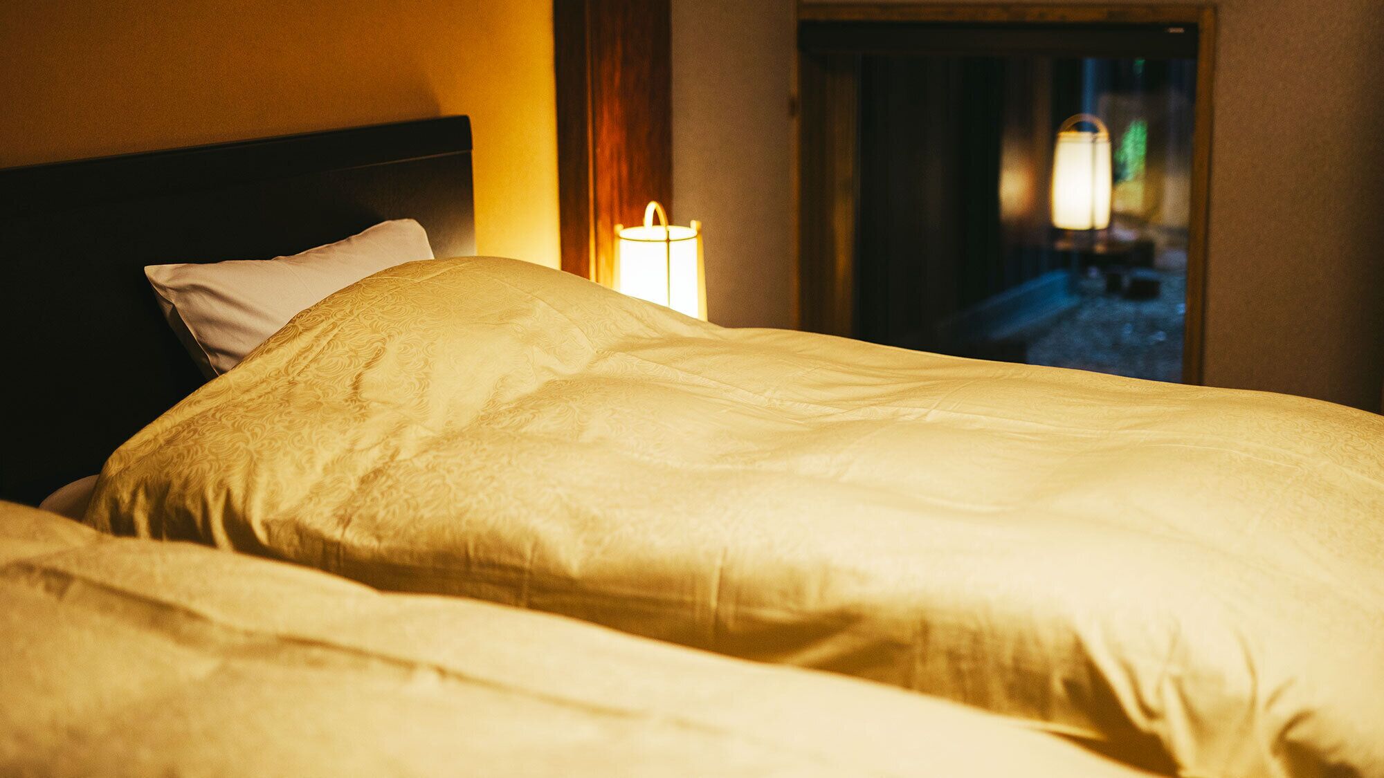 A bed with a headboard and a bedside lamp in a hotel room.