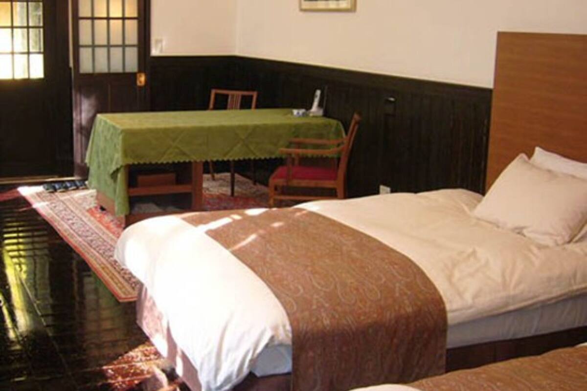 A room with two beds, a table with a green tablecloth, and a chair.