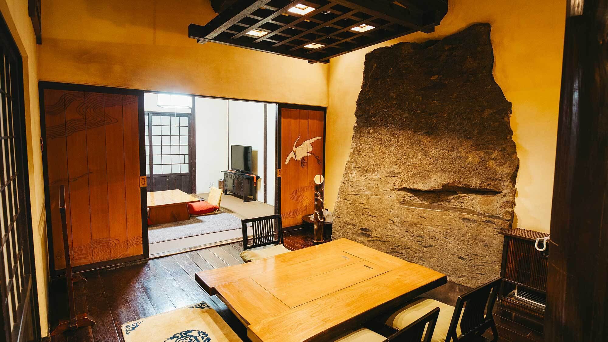A traditional Japanese room with tatami flooring, a low wooden table, sliding doors, and a stone wall.