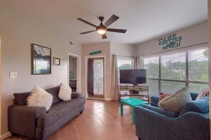 A living room with a sofa, a TV, a ceiling fan, and a sign that reads 'LIFE COTTING RIVER.' - IC 302 Ripley River Haus (New Braunfels)