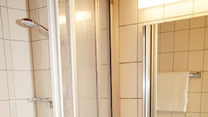 Een badkamer met een douchecabine van glas, een witte wastafel en een spiegel boven de wastafel.