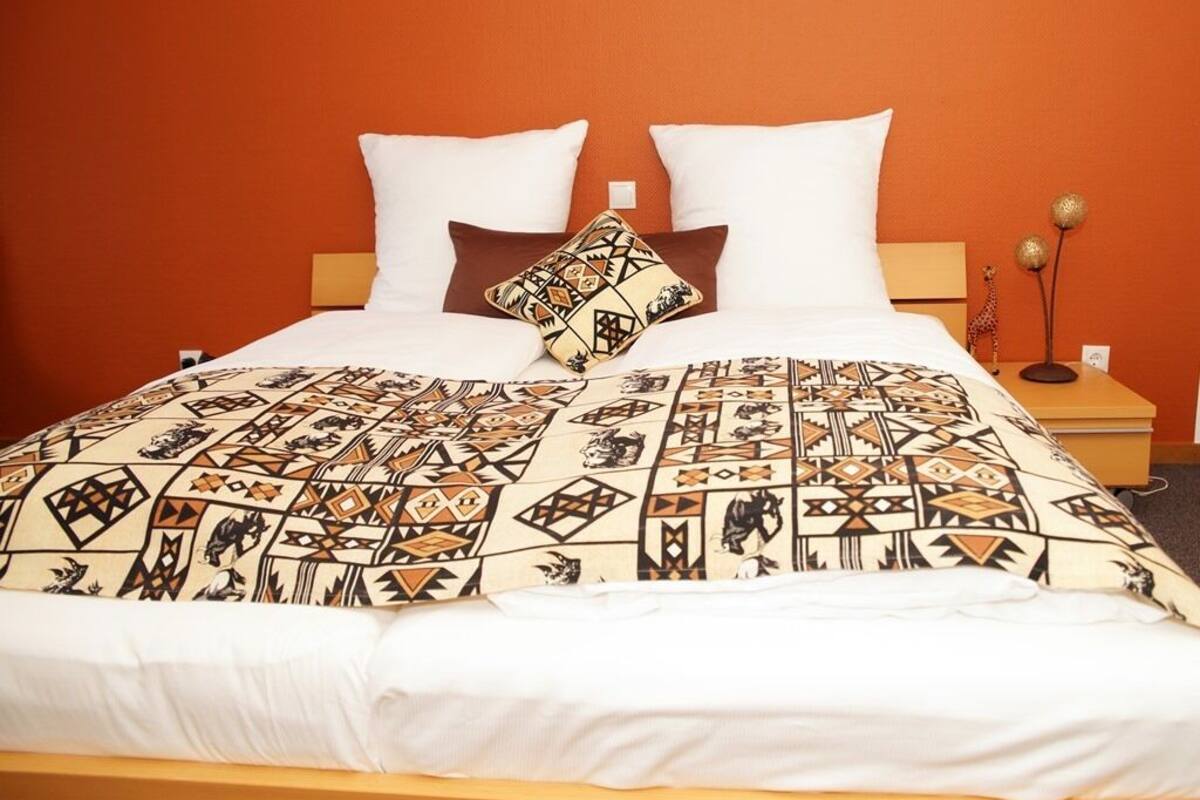 Un lit recouvert d’une couvre-lit à motifs, avec deux oreillers blancs et un coussin décoratif à motifs géométriques.