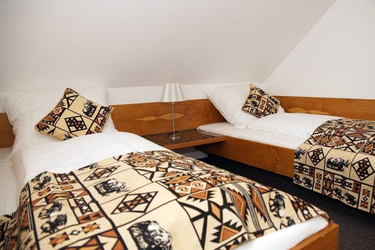 Une chambre avec deux lits, chacun agrémenté de draps et d’oreillers à motifs. Une petite table avec une lampe se trouve entre les deux lits.