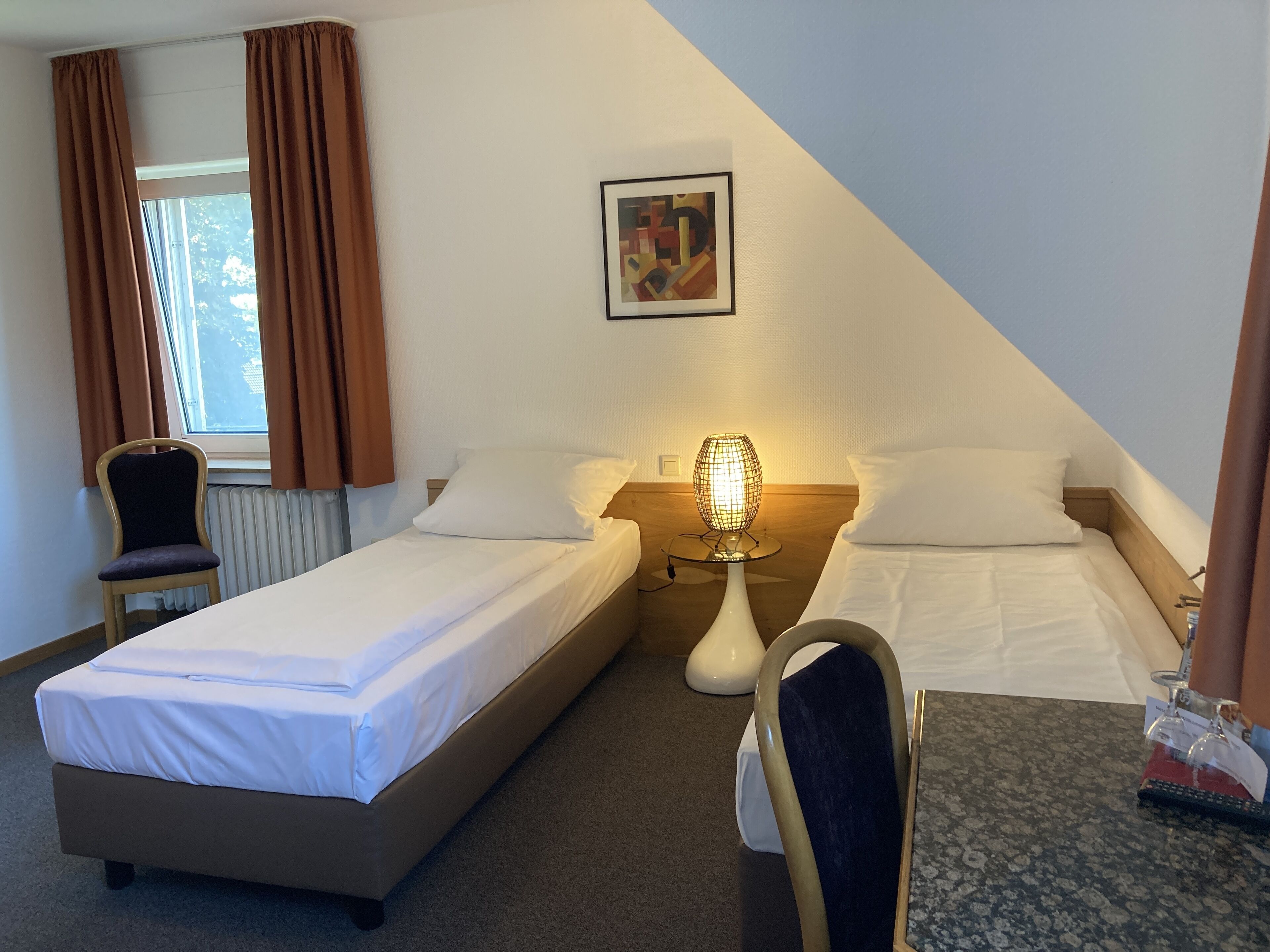 Une chambre d’hôtel avec deux lits simples, une chaise, une table, une lampe et un tableau au mur.