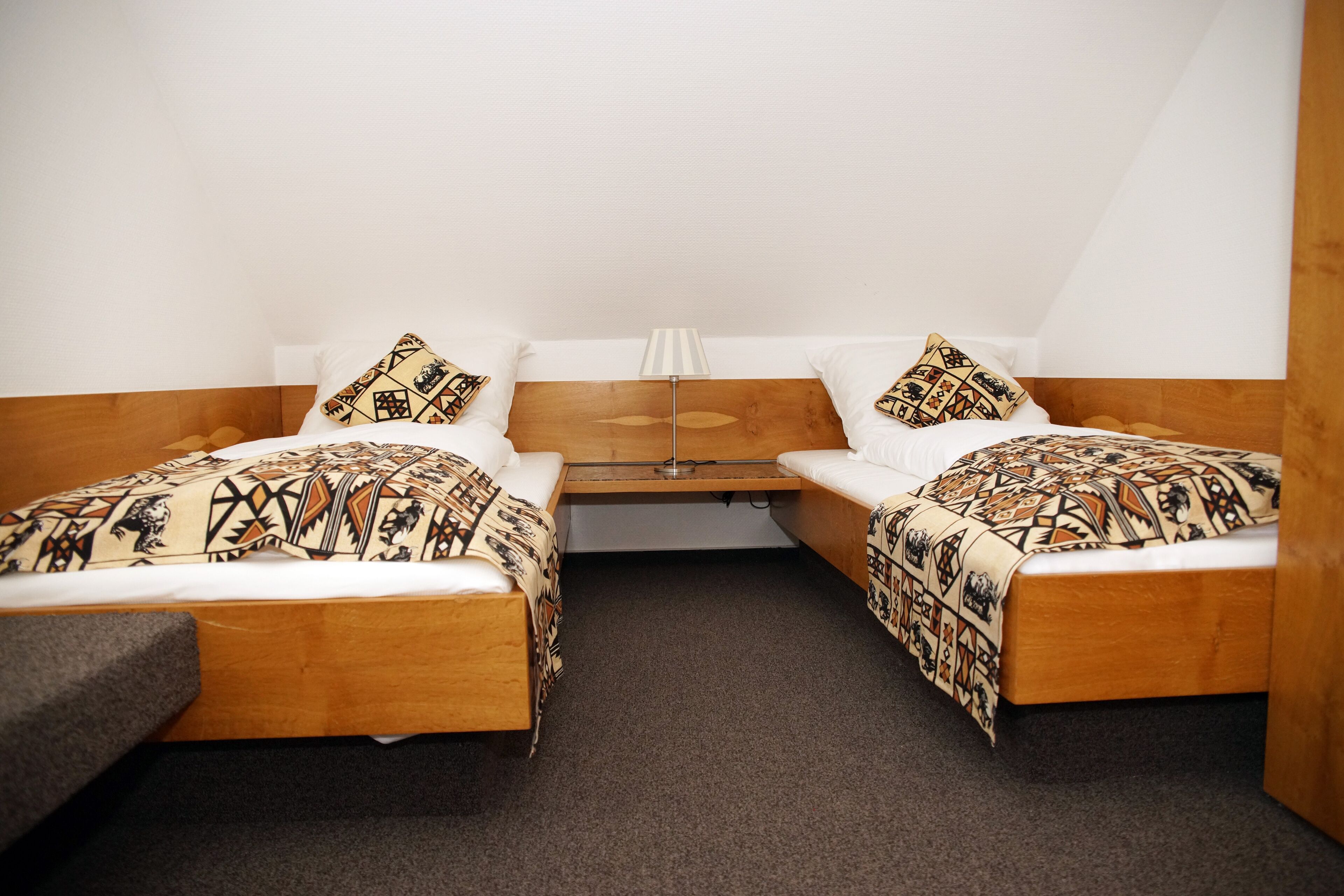 Ein Doppelzimmer mit zwei Einzelbetten, einem Holzkopfende, einem kleinen Tisch und einer Lampe.