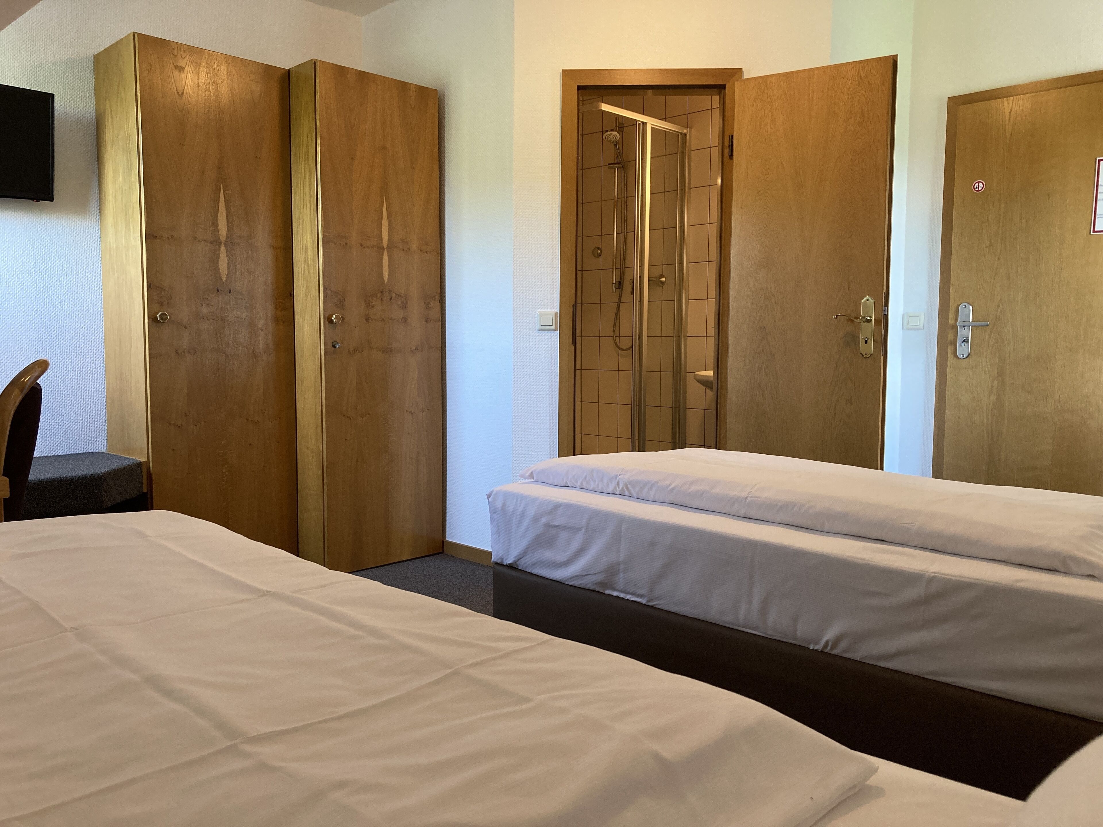 Ein Hotelzimmer mit zwei Betten, Holzschränken, einer Duschkabine und einem an der Wand befestigten Fernseher.