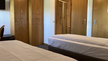 Ein Hotelzimmer mit zwei Betten, Holzschränken, einer Duschkabine und einem an der Wand befestigten Fernseher.