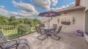Un balcon doté d’une table et de chaises en verre, d’un parasol, d’appliques murales décoratives et offrant une vue sur un paysage verdoyant.