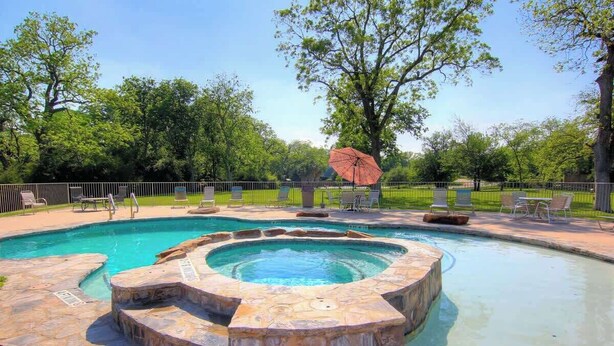 Une piscine avec un jacuzzi, entourée d’escaliers en pierre et d’une clôture.