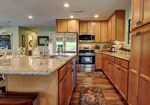 Una cocina con armarios de madera, electrodomésticos de acero inoxidable, encimera de mármol y alfombra estampada.