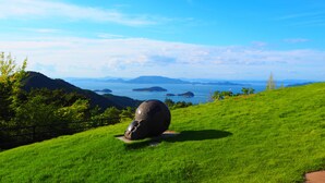 Una colina cubierta de hierba con una gran escultura de roca en primer plano y una vista panorámica del mar y unas islas en la distancia.