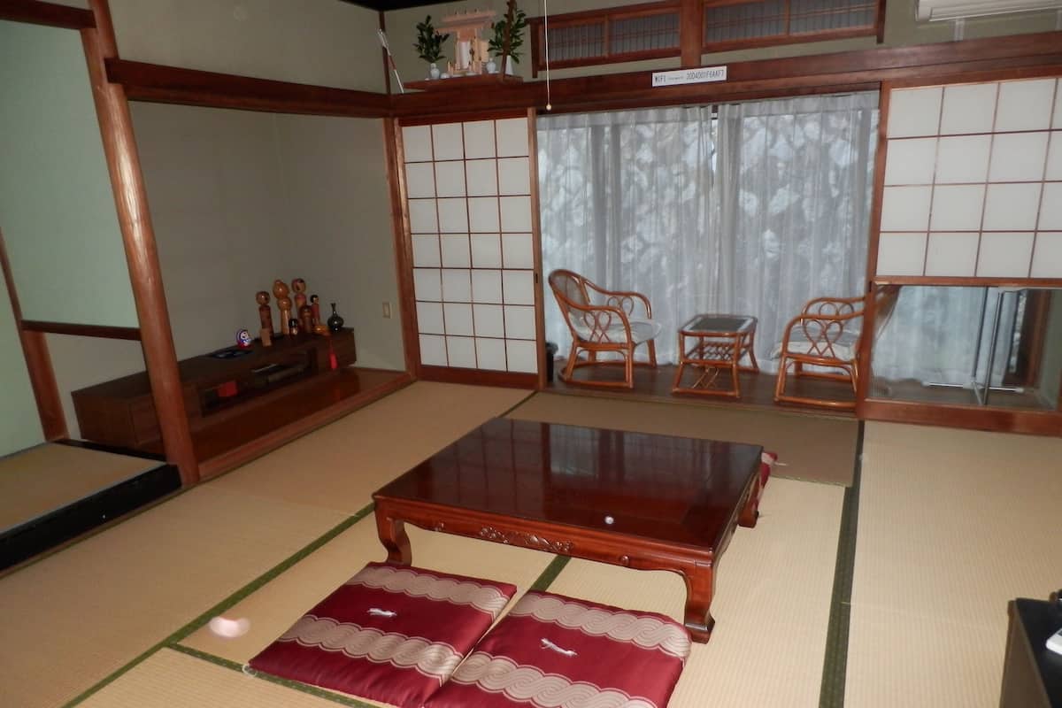 Una habitación con tatamis, una mesa baja de madera y cojines, muebles tradicionales japoneses y un fusuma con un diseño de cuadrícula.