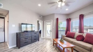 A living room with a TV, wooden furniture, a ceiling fan, and a sliding glass door leading to a balcony.